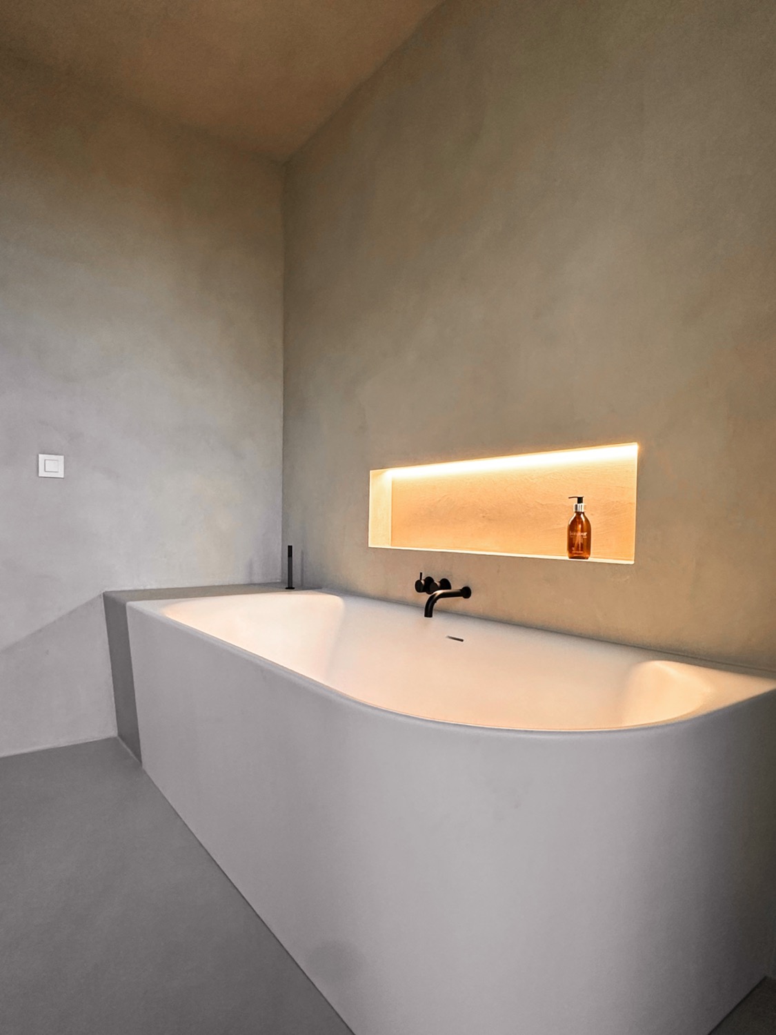 Stijlvoorbeeld microcement badkamer bad in nis met indirect licht
