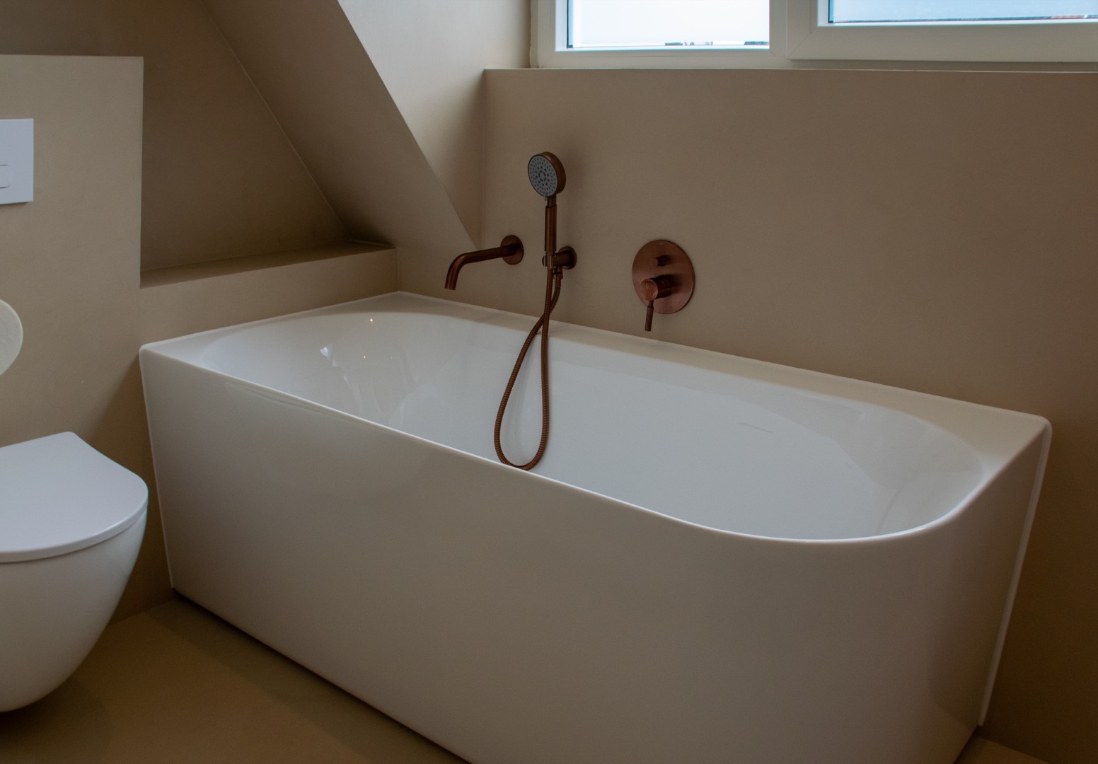 Stijlvoorbeeld microcement badkamer bad en toilet onder dakkapel